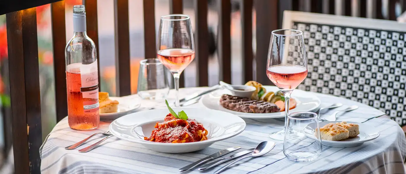 Una tavola imbandita con pasta, carne e vino rosé